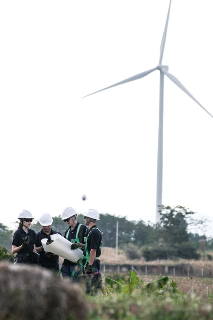 Técnicos con casco revisando planos junto a un aerogenerador